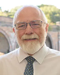 Michael Brett, white beard and glasses, smiling, brick arches behind
